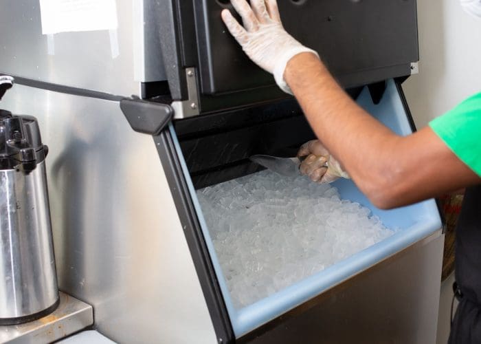 A view of an employee scooping ice out of an ice machine, in a restaurant setting.